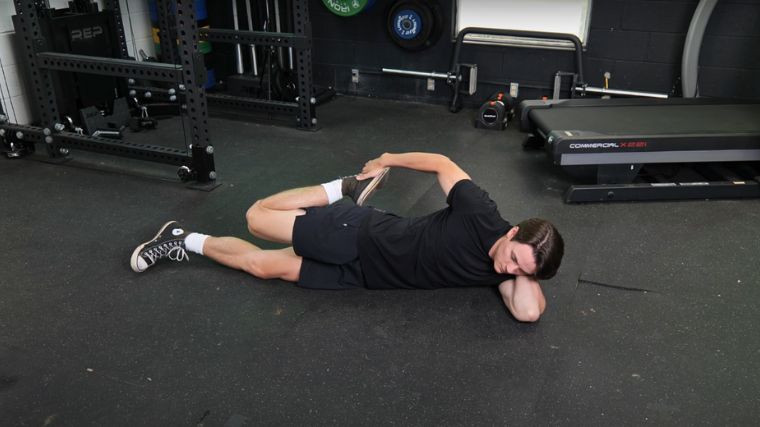 BarBend's Jake Herod performing the lying quad stretch.